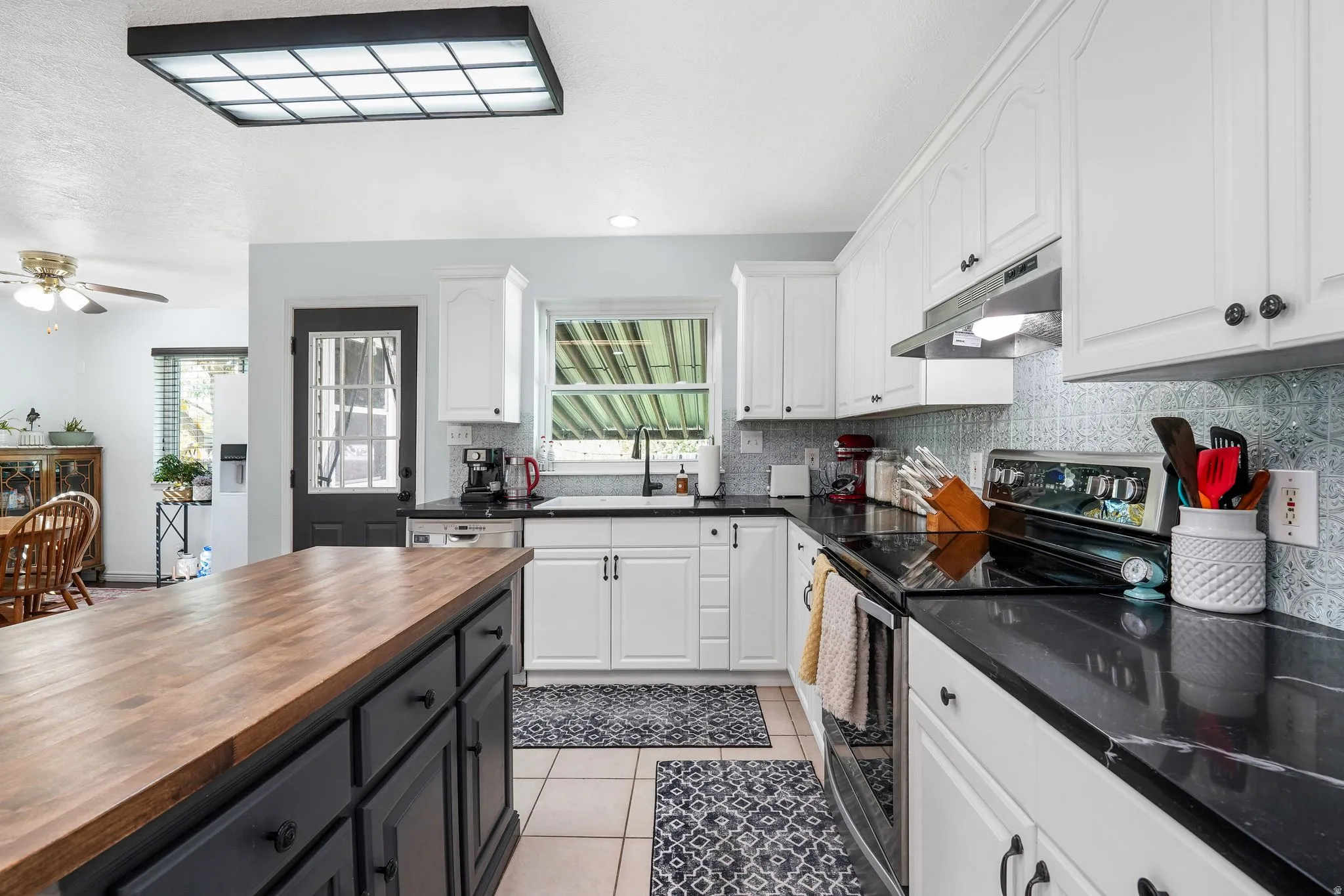 Kitchen featuring two tone cabinets, stainless steel appliances, wooden counters, light tile patterned floors, and healthy amount of natural light