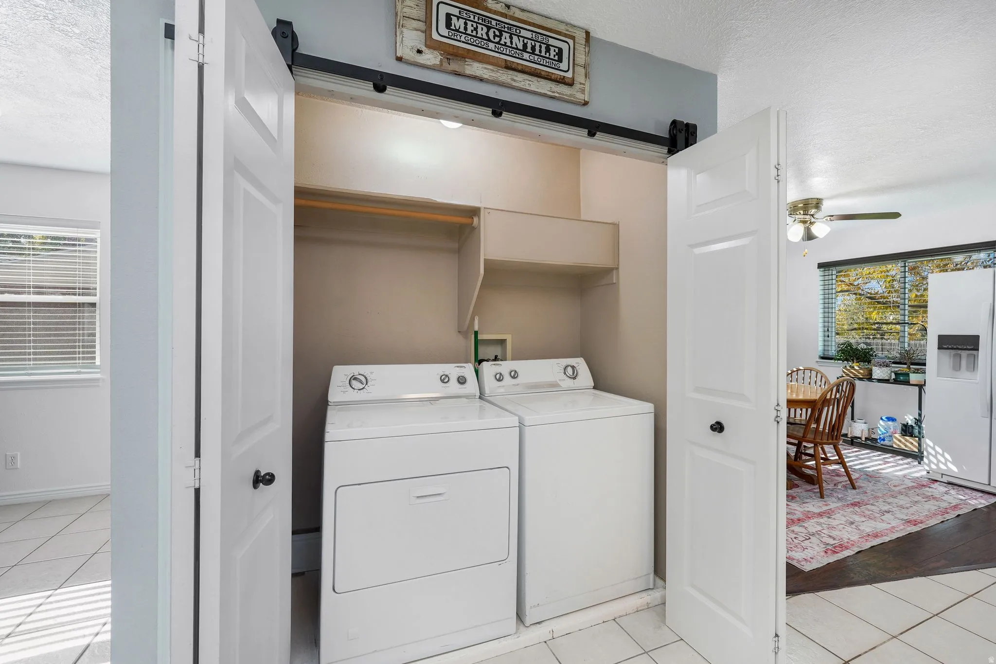 Laundry area with a textured ceiling, light tile patterned floors, a ceiling fan, a barn door, and washing machine and dryer