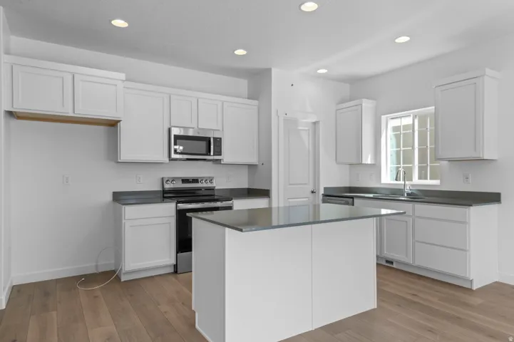 Kitchen with stainless steel appliances, white cabinets, dark countertops, light wood-style floors, and recessed lighting