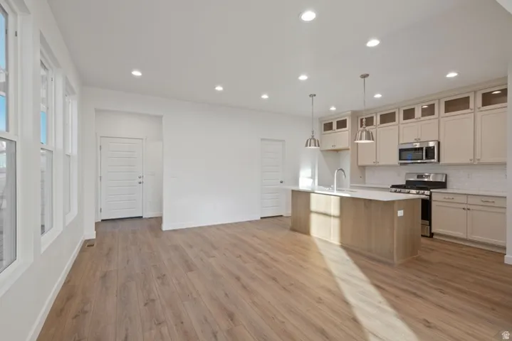 Dual tone kitchen featuring stainless steel appliances, a center island with sink, glass insert cabinets, light wood-style floors, and pendant lighting