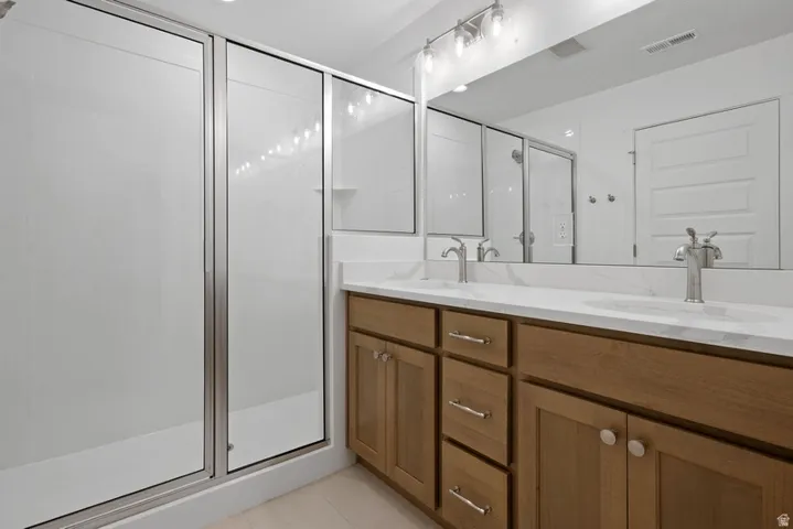 Bathroom featuring double vanity, a stall shower, and light tile patterned floors