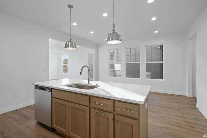 Kitchen with wood finish cabinetry, pendant lighting, stainless steel dishwasher, light wood-type flooring, and a center island with sink