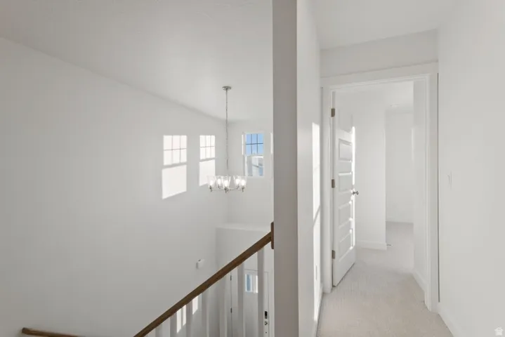 Corridor featuring light colored carpet, a chandelier, and an upstairs landing