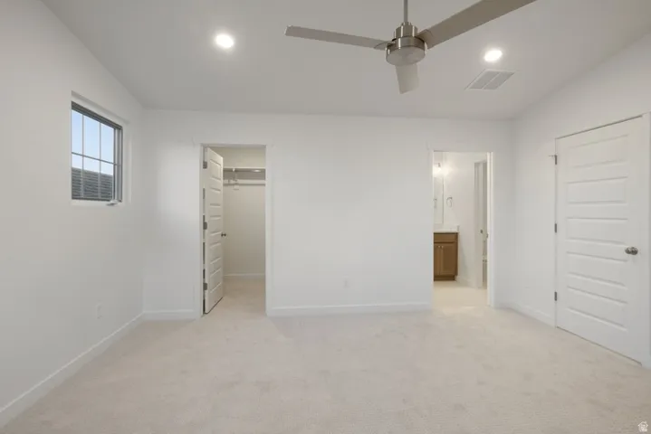 Unfurnished bedroom with light carpet, a spacious closet, a ceiling fan, connected bathroom, and recessed lighting