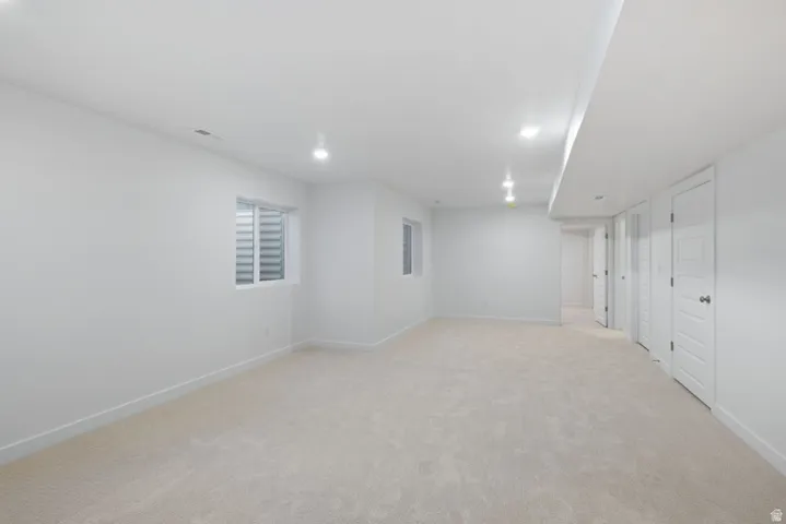 Finished below grade area featuring light colored carpet and recessed lighting