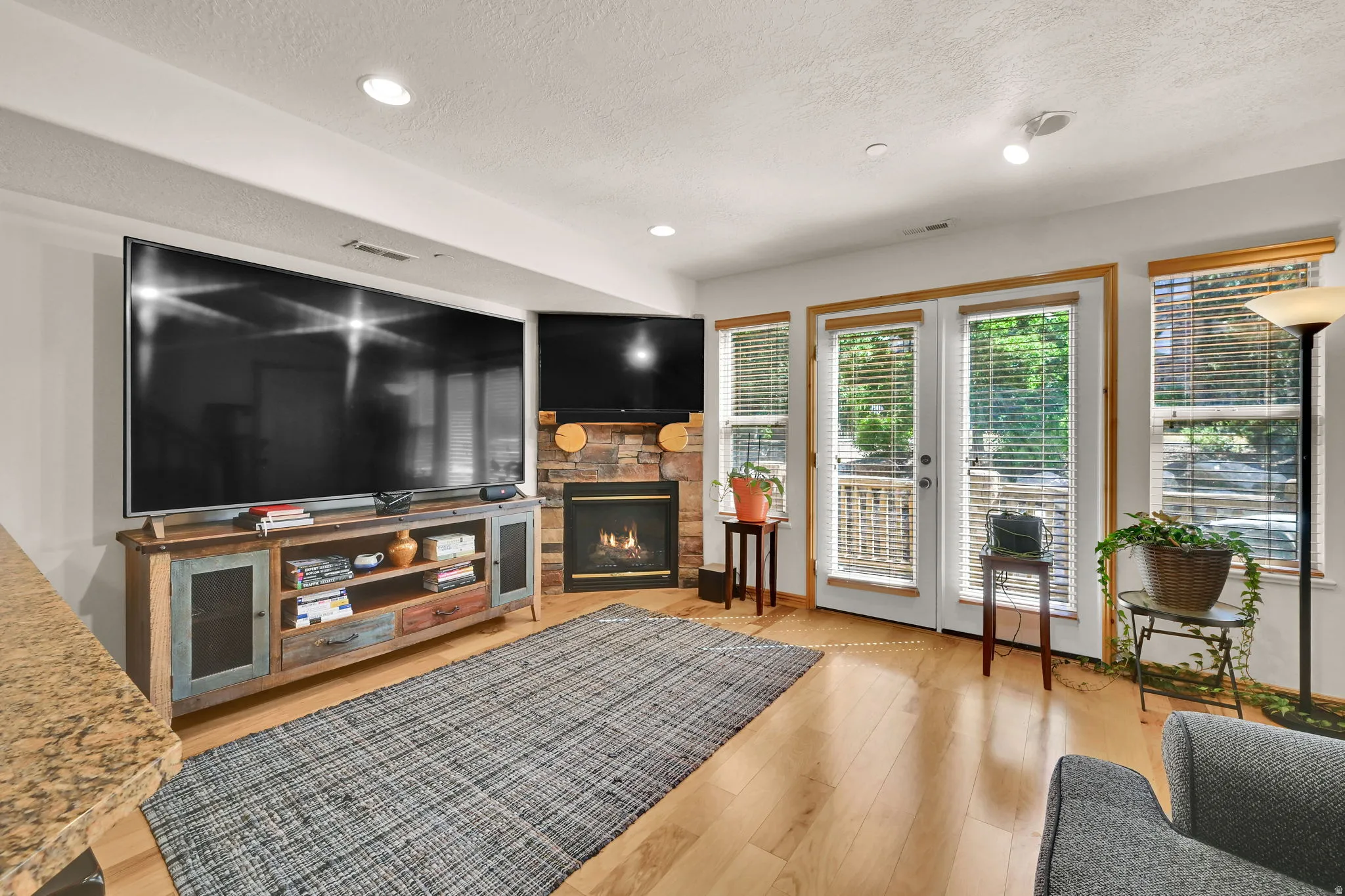 Living area with light wood-type flooring, a fireplace, french doors, recessed lighting, and a textured ceiling
