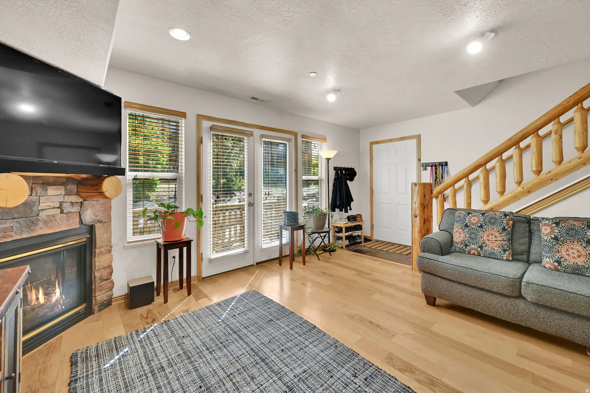 Living room featuring light wood-style floors, a textured ceiling, a stone fireplace, and recessed lighting