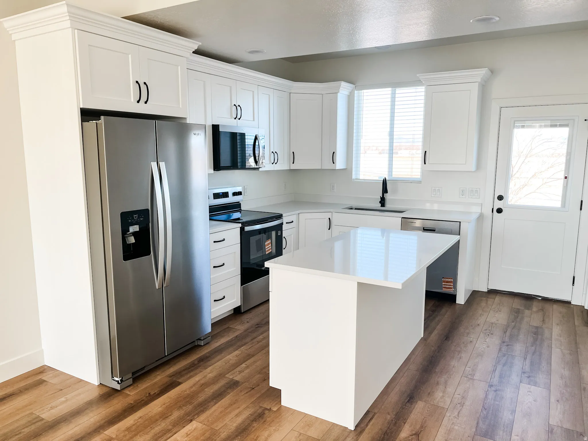 Kitchen with stainless steel appliances, white cabinetry, a center island, and dark wood-type flooring