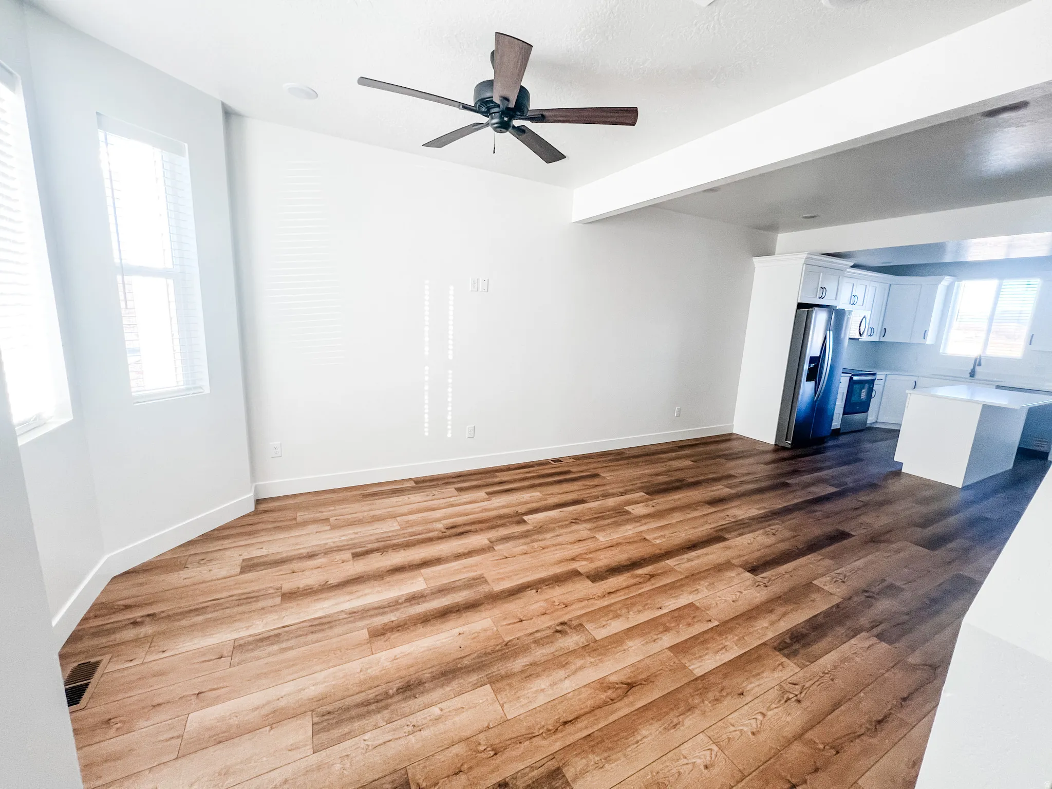 Unfurnished living room featuring dark wood-type flooring, a ceiling fan, and beam ceiling