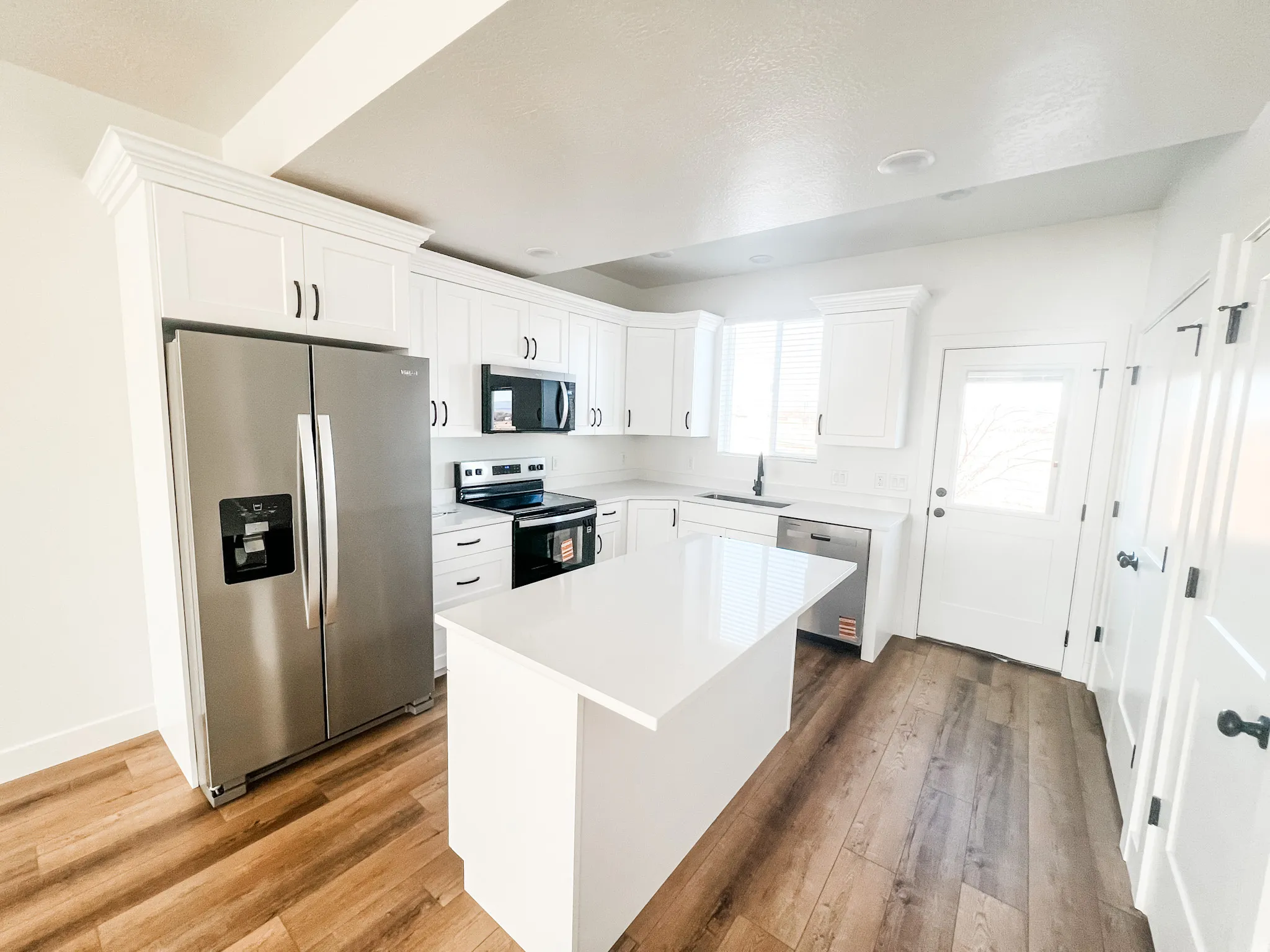 Kitchen with stainless steel appliances, white cabinets, dark wood-style floors, a center island, and light stone countertops
