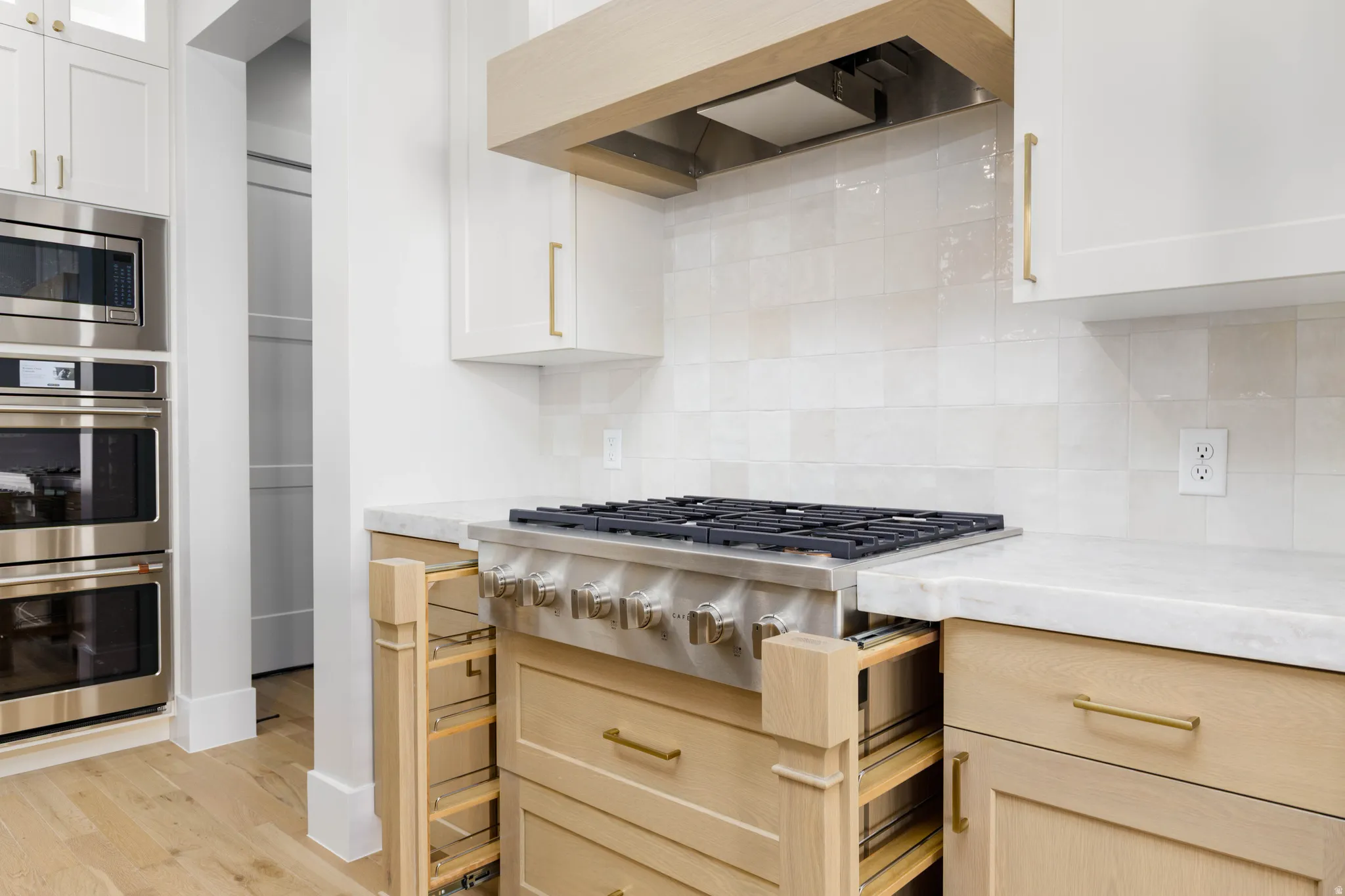 Kitchen with stainless steel appliances, glass fronted cabinets, light stone countertops, and white cabinets
