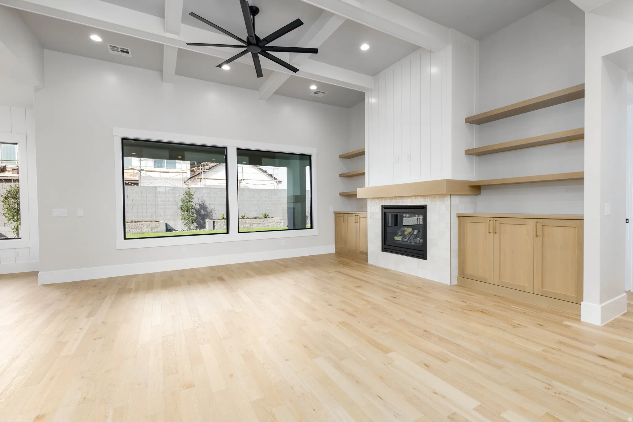 Unfurnished living room featuring a ceiling fan, light wood finished floors, beamed ceiling, a fireplace, and recessed lighting