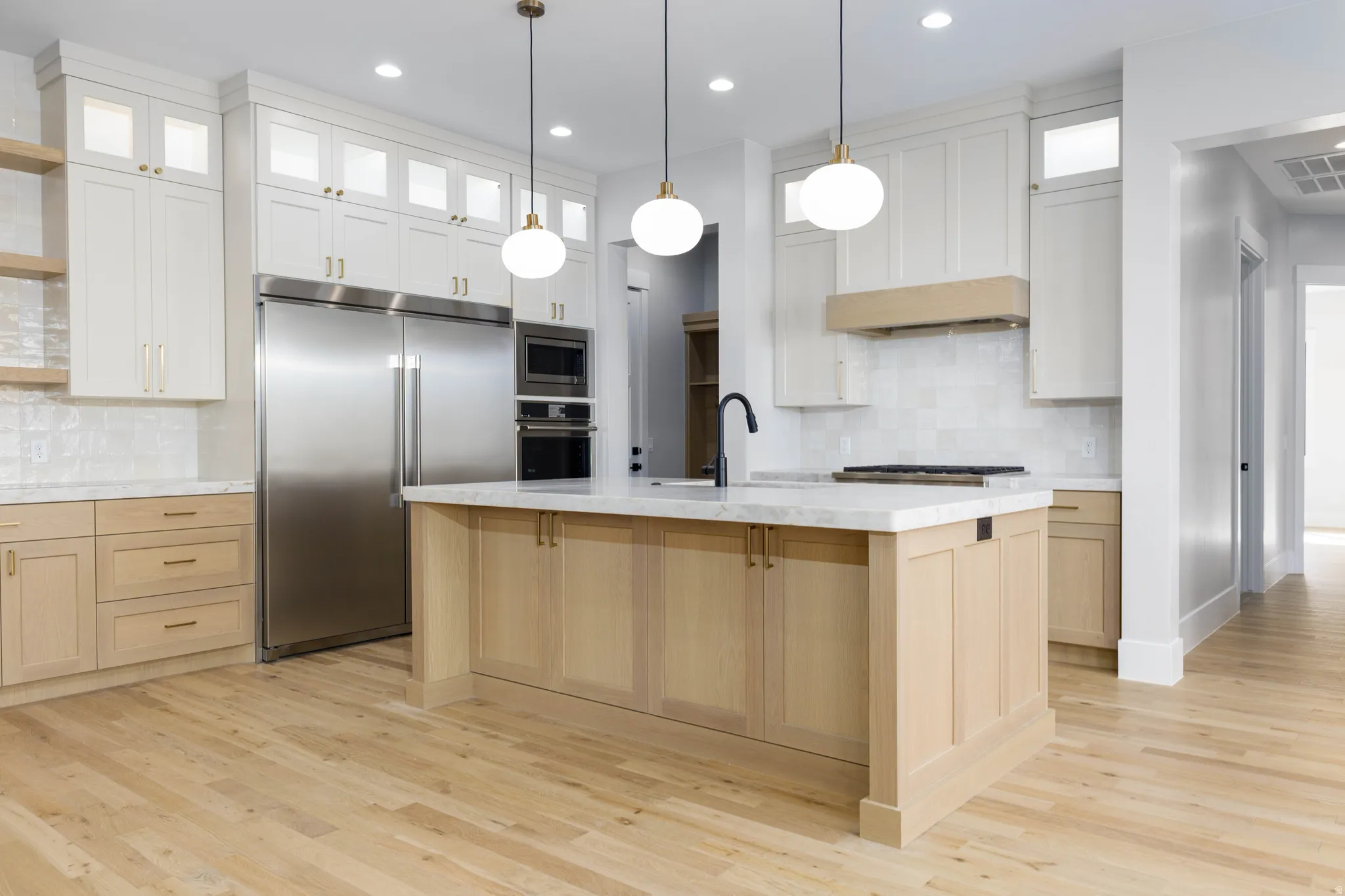 Kitchen with glass insert cabinets, built in appliances, backsplash, light wood-style flooring, and dual tone cabinets