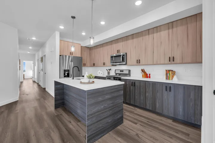 Nicely appointed kitchen featuring an island with sink, decorative light fixtures, modern cabinets, stainless steel appliances, and light quartz countertops