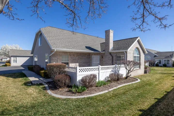View of front of condo featuring brick siding, a front yard, a shingled roof, and a chimney