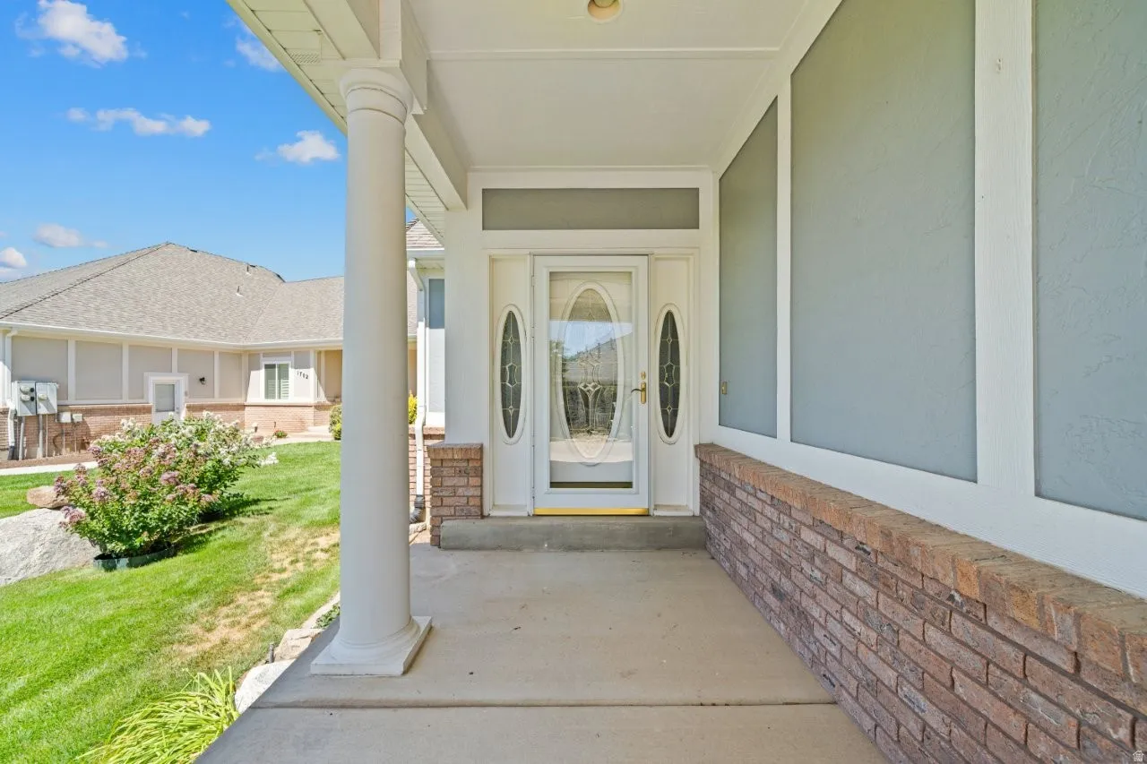 Property entrance with a porch, stucco siding, and a lawn