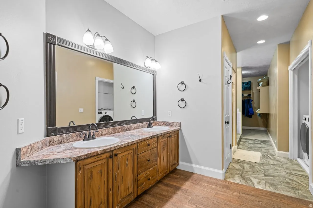Bathroom with double vanity, a spacious closet, light wood-style flooring, and recessed lighting