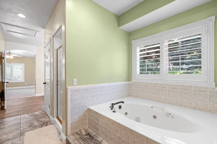 Bathroom featuring a stall shower, a tub with jets, tile walls, and a wainscoted wall