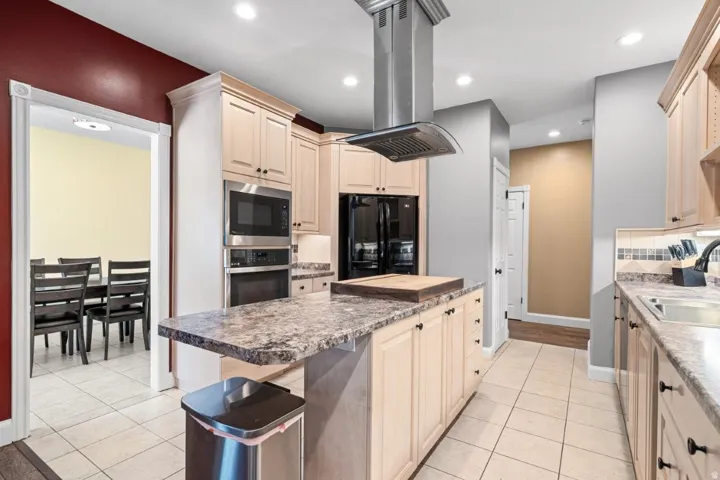 Kitchen featuring island exhaust hood, stainless steel appliances, a kitchen island, light tile patterned floors, and recessed lighting