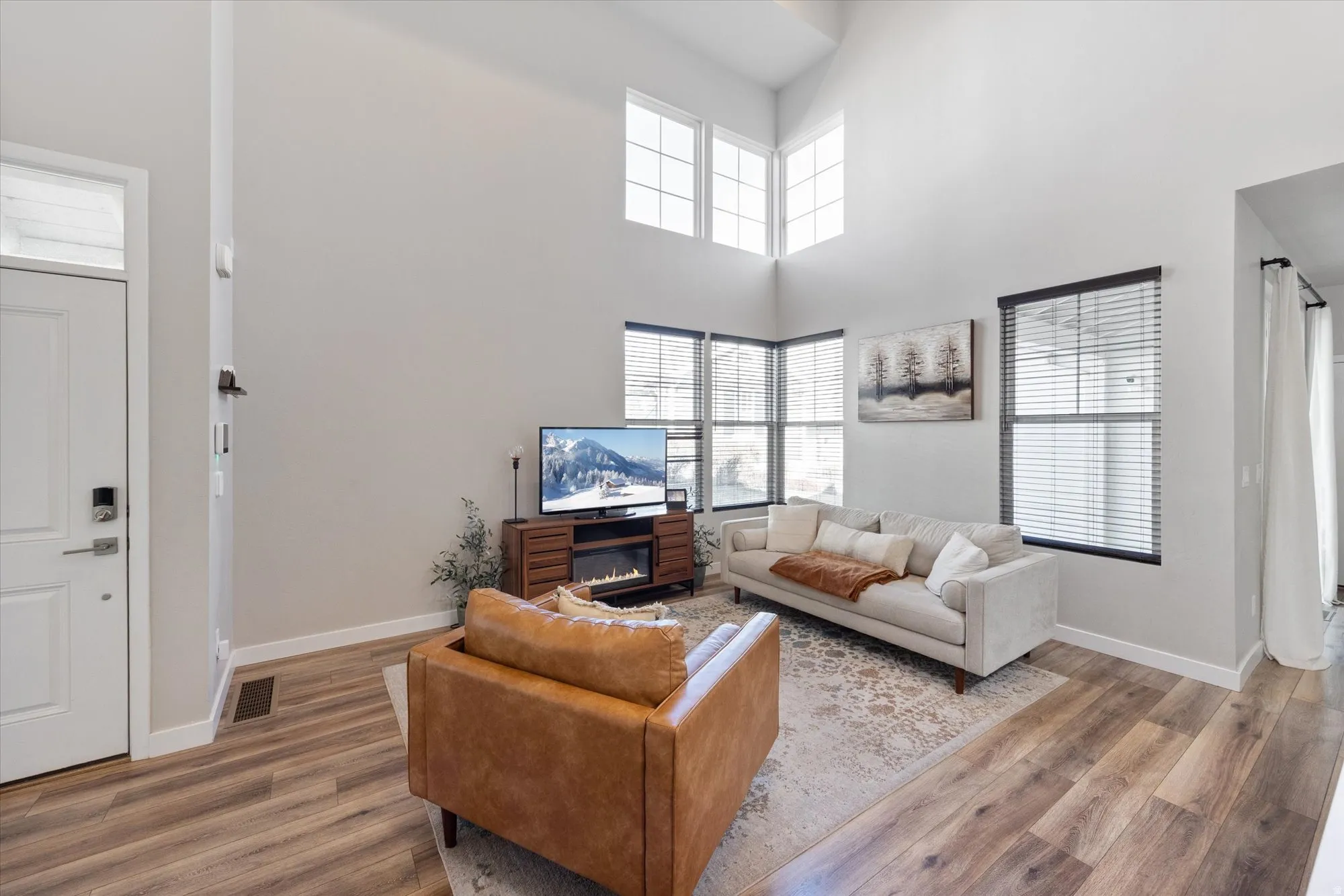 Living room featuring wood finished floors, a high ceiling, and a glass covered fireplace