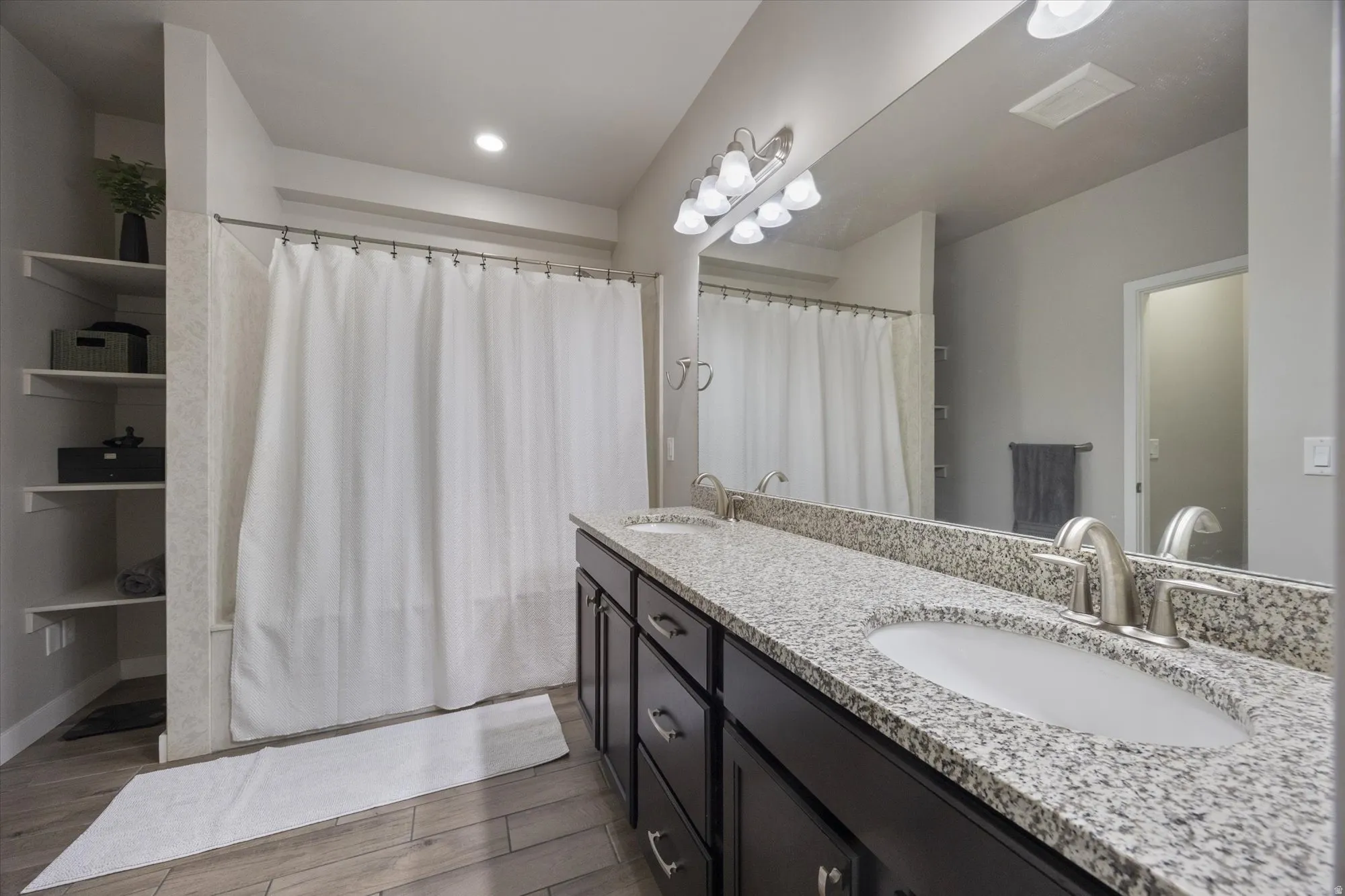 Full bath with double vanity, a shower with shower curtain, and light wood finished floors