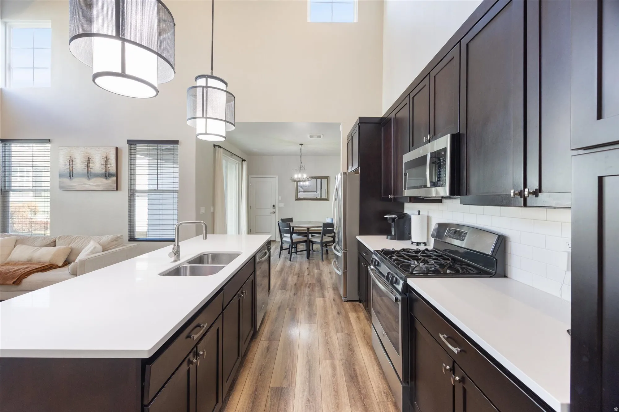 Kitchen featuring dark wood finish cabinetry, stainless steel appliances, open floor plan, light wood finished floors, and a high ceiling