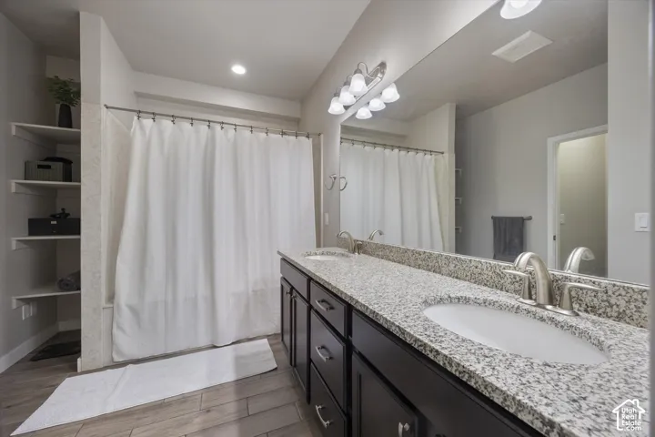 Full bath with double vanity, a shower with shower curtain, and light wood finished floors