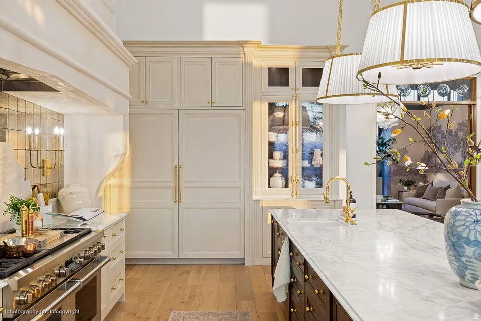 Kitchen with dual tone cabinets, double oven range, light stone countertops, light wood-type flooring, and glass fronted cabinets