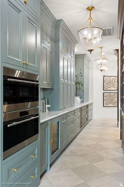 Bar with stainless steel double oven, hanging lights, beverage cooler, and light stone counters