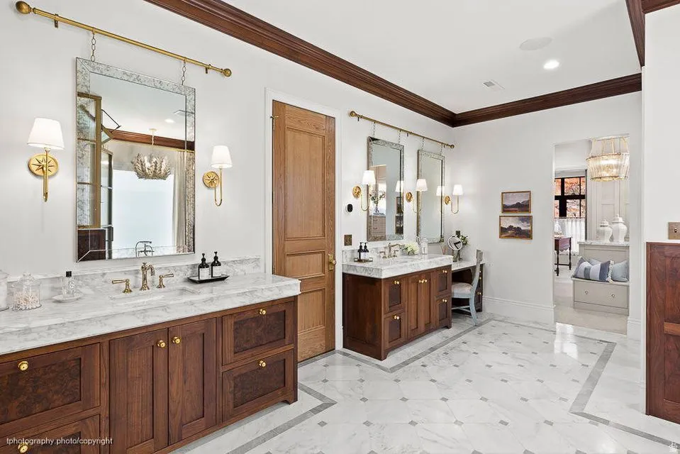 Full bath featuring inlaid floor details, a chandelier, ensuite bathroom, two vanities, and crown molding
