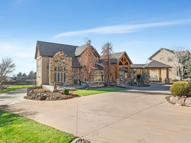 Stone and stucco exterior, prominent gabled rooflines, covered entry with exposed wood beams, attached covered walkway, and expansive paved driveway