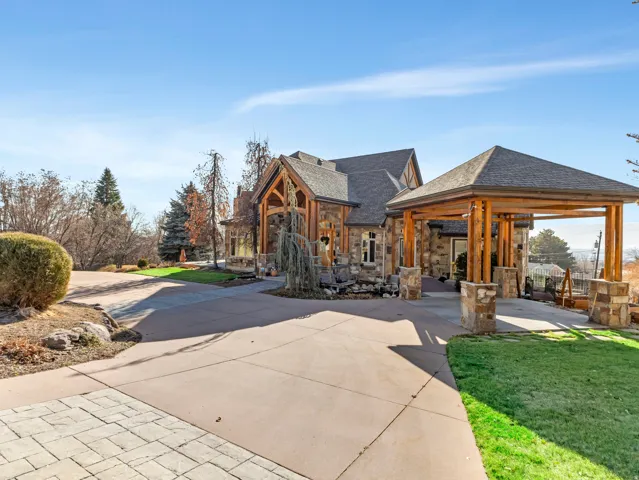 Stone and wood-beam exterior featuring a covered porte-cochère, paved driveway, and manicured landscaping