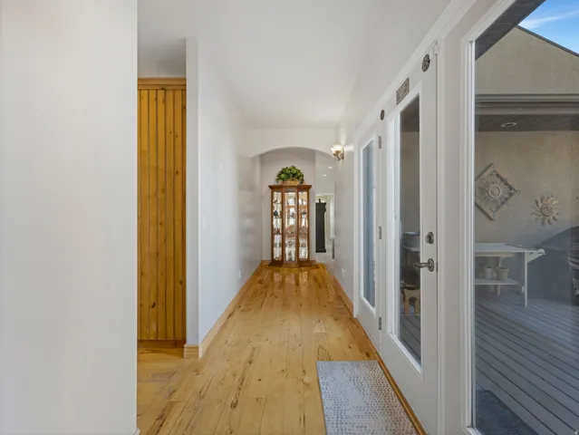 Corridor featuring light wood finished floors, french doors, arched walkways, and plenty of natural light