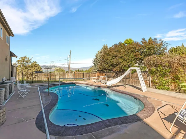 Freeform swimming pool featuring a white slide and expansive concrete decking
