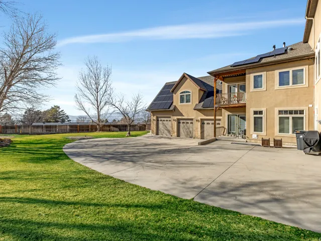Expansive concrete driveway, attached three-car garage, upper-level balcony, and multiple solar panels