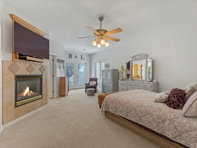 Bedroom featuring french doors, access to outside, a tiled fireplace, ceiling fan, and carpet flooring