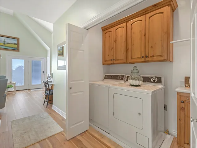 Laundry room featuring cabinet space, light wood-style floors, washer and clothes dryer, and vaulted ceiling