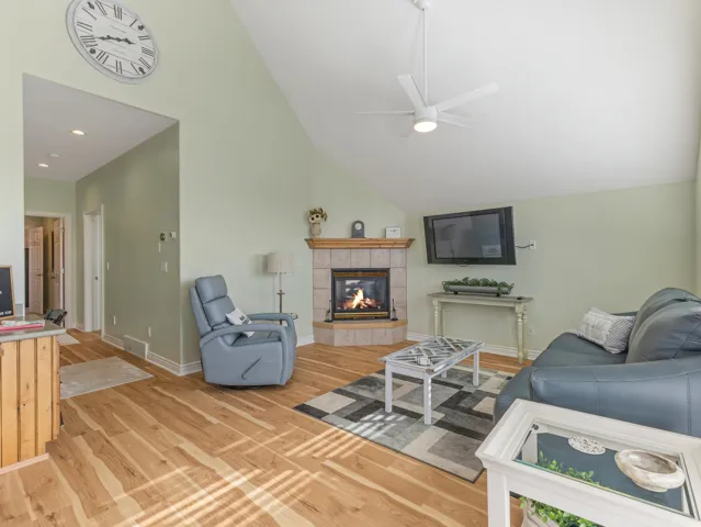 Living area featuring a tiled fireplace, ceiling fan, light wood finished floors, and vaulted ceiling