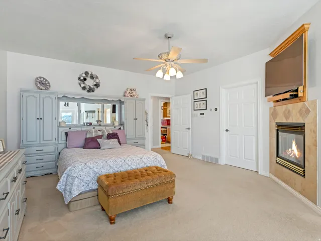 Bedroom with a tiled fireplace, light colored carpet, and ceiling fan