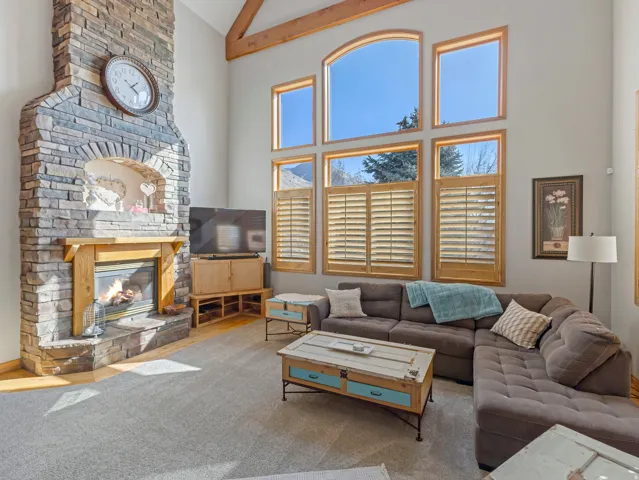 Living area with a stone fireplace, carpet flooring, and vaulted ceiling