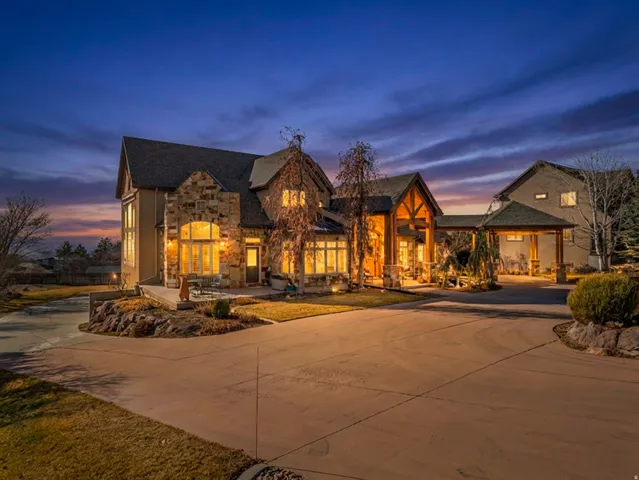 View of front of home with curved driveway, stone siding, and roof with shingles