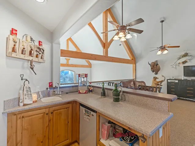 Kitchen featuring open floor plan, dishwasher, a peninsula, light stone countertops, and vaulted ceiling