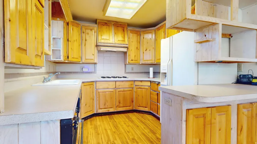Kitchen with open shelves, light countertops, decorative backsplash, light wood-type flooring, and white refrigerator with ice dispenser