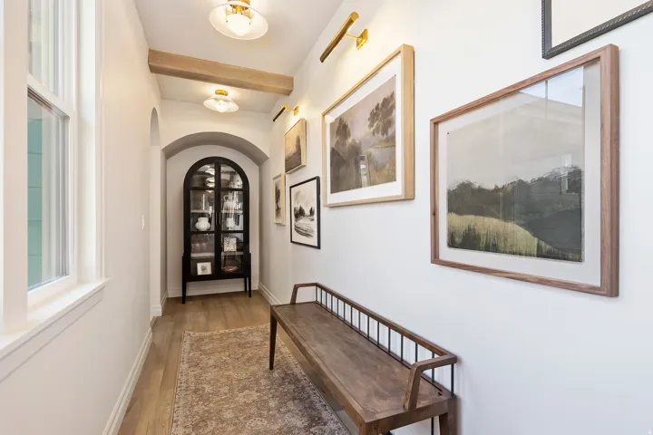 Hallway with light wood-type flooring, arched walkways, and beam ceiling