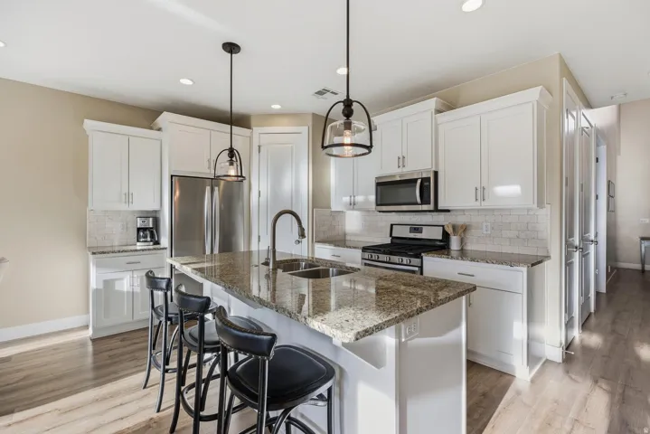 Kitchen featuring dark stone countertops, stainless steel appliances, light wood-style floors, white cabinets, and a breakfast bar