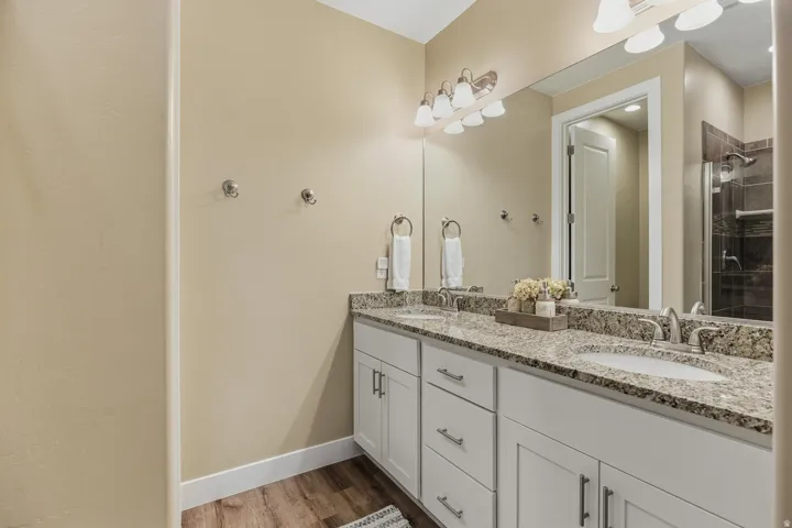 Full bath with double vanity, a stall shower, and light wood-style flooring
