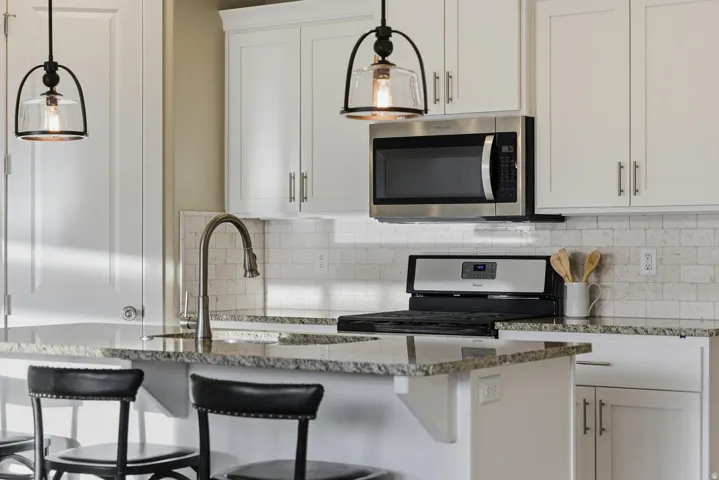 Kitchen with white cabinetry, stainless steel appliances, pendant lighting, and dark stone countertops