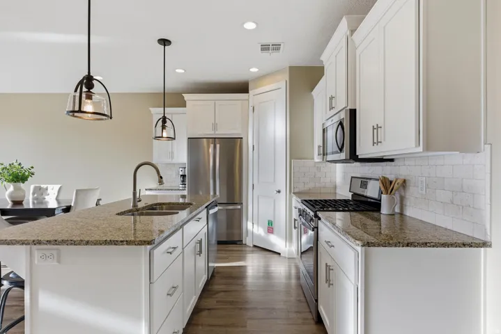 Kitchen with a breakfast bar area, stainless steel appliances, pendant lighting, dark stone counters, and white cabinetry