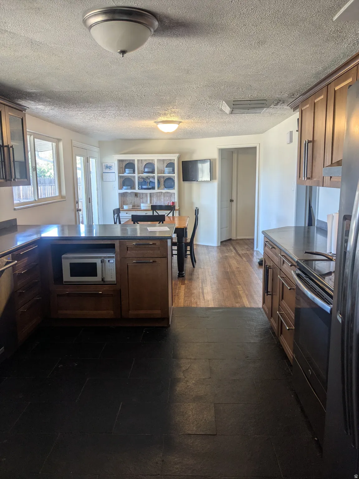 Kitchen with a peninsula, wood finish cabinetry, dark countertops, stainless steel appliances, and a textured ceiling