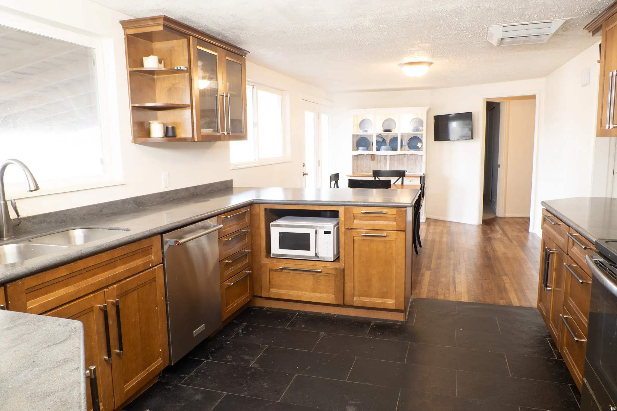 Kitchen featuring glass insert cabinets, a peninsula, wood finish cabinets, open shelves, and stainless steel dishwasher